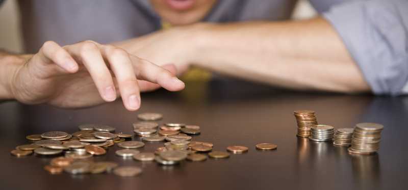 Person counting stacks of coins on table surface.