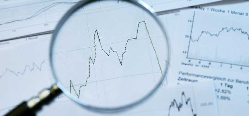 Stock charts and sheets of data under magnifying glass