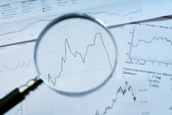 Stock charts and sheets of data under magnifying glass