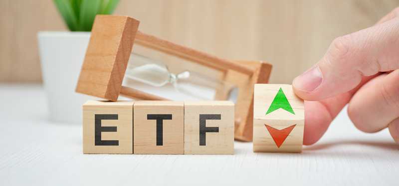 Wooden blocks on a table that spell ETF next to wooden block with green and red arrows in front of an hourglass.