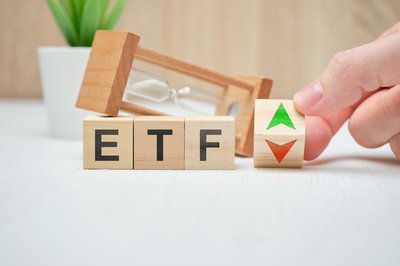 Wooden blocks on a table that spell ETF next to wooden block with green and red arrows in front of an hourglass.