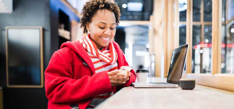Person sitting in coffee shop and smiling and looking at phone.