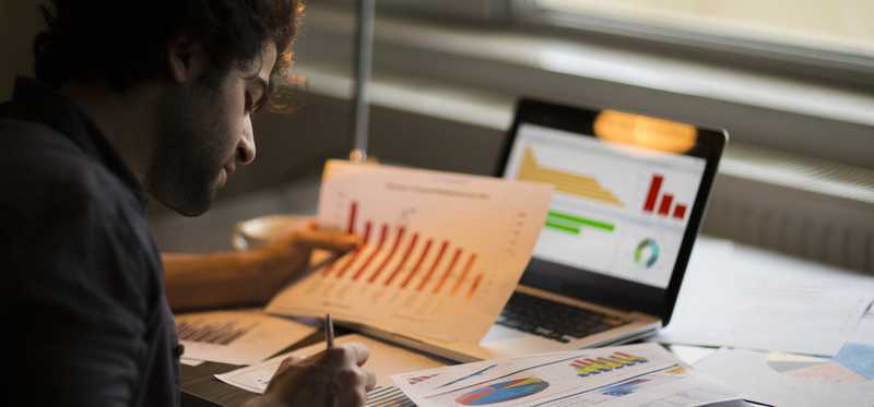 Person reviewing charts on paper and laptop in dark office.