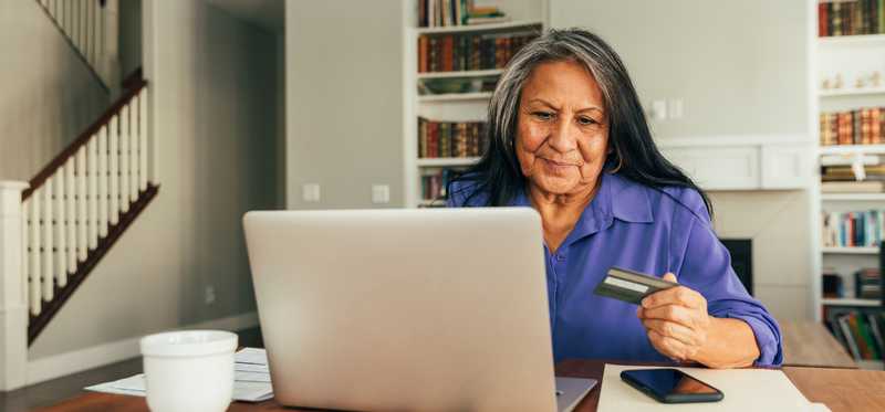 Person holding debit or credit card while looking at laptop.