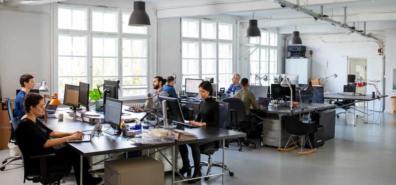 Workers sitting at desks in trendy office setting with large windows and high ceilings.