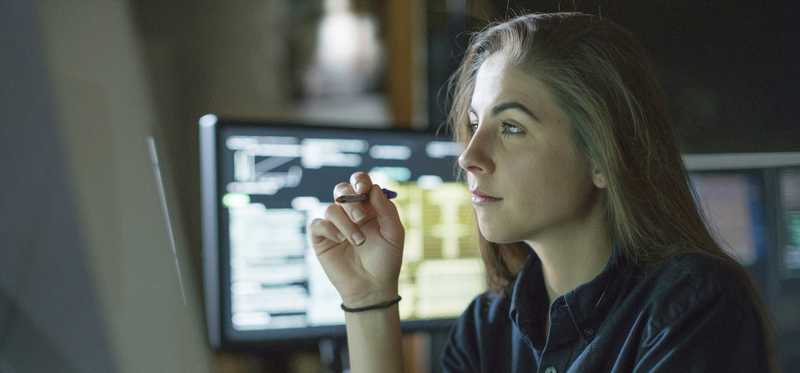 Young woman in darkened room and glowing in light of dual screen monitors