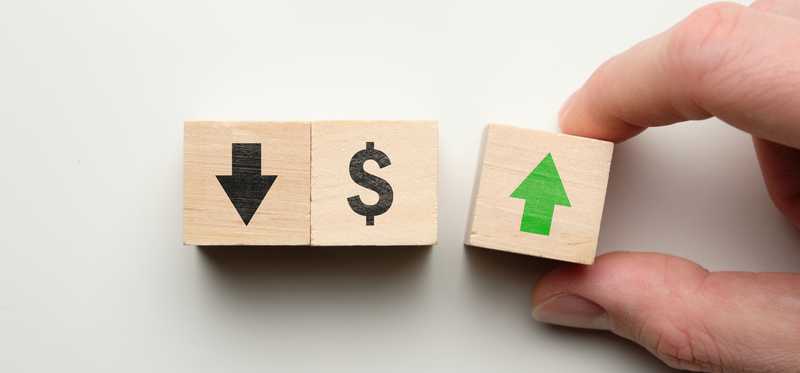 Hand holds block with green up arrow next to blocks with black down arrow and dollar sign.