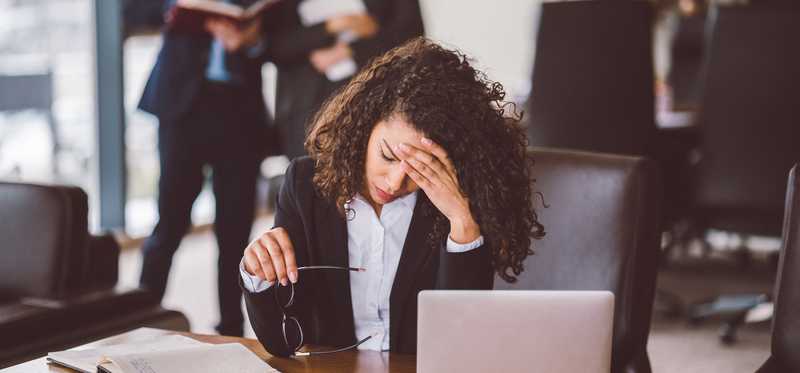 Person holding glasses and rubbing forehead worriedly in an office.
