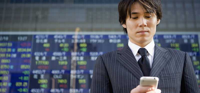 Investor looking at phone against background of stock charts