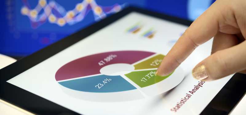Hand of person reviewing asset allocation on tablet against backdrop of market movements.