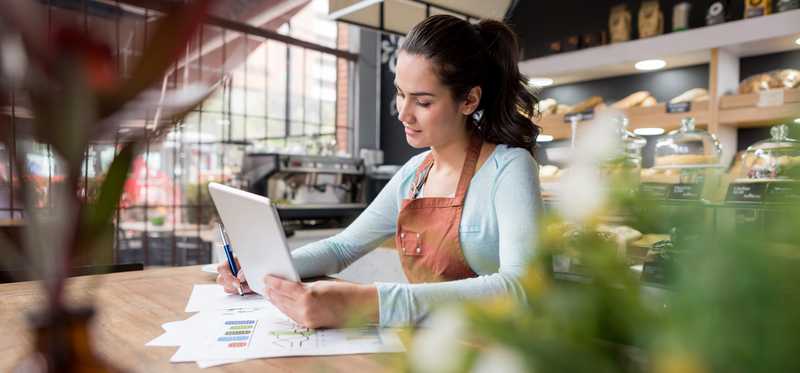 Woman looking at financial documents and tablet while sitting in coffee shop