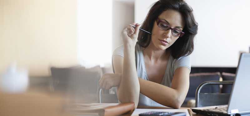 Person holding pen and looking thoughtfully at notebook and calculator.