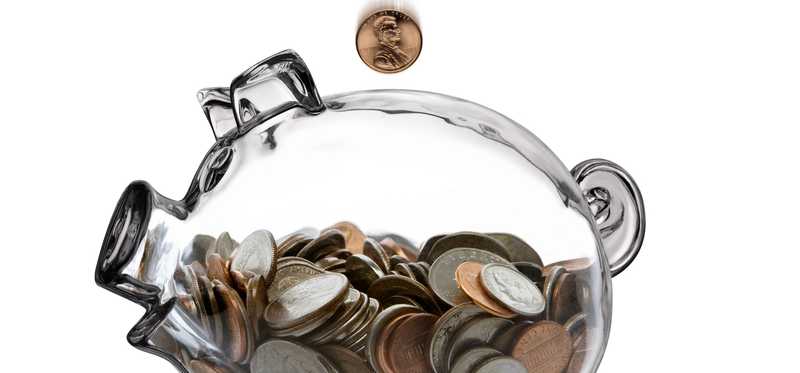 Person putting coins in clear glass piggy bank