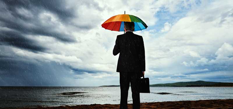 Barefoot person on beach is looking at stormy horizon while holding umbrella.