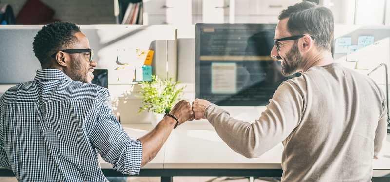 Coworkers sitting at their desk fist-bumping each other