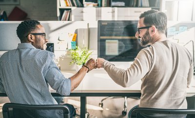 Coworkers sitting at their desk fist-bumping each other