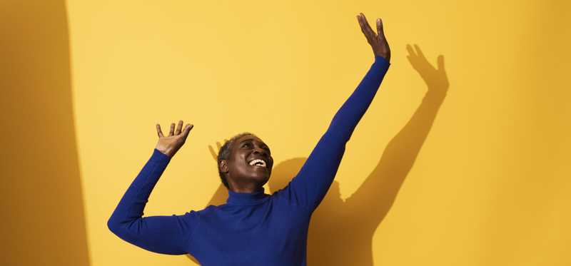 Happy person jumping for joy against bright orange yellow background.