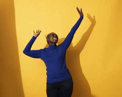 Happy person jumping for joy against bright orange yellow background.