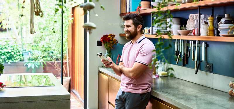 Person leaning on kitchen counter is smiling while looking at phone.