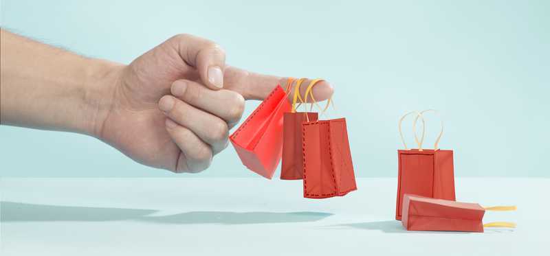 Hand holding small red shopping bags against light blue background
