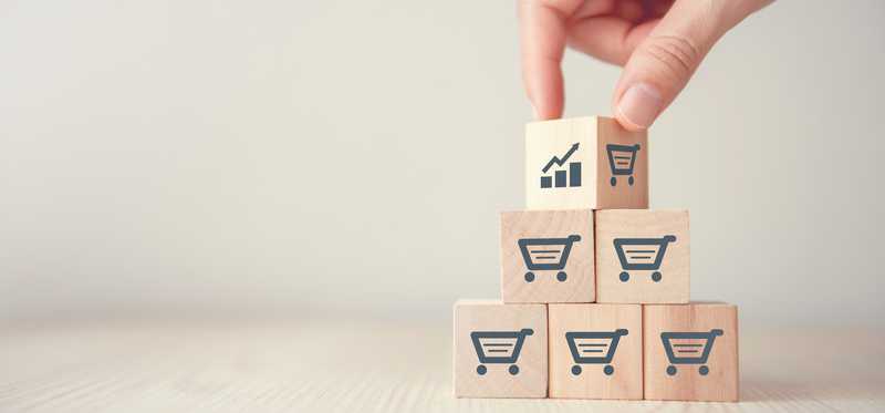 Hand stacking wooden blocks with images of shopping carts and trending growth