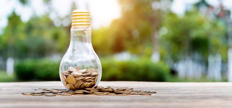 Lightbulb on wooden table filled with and surrounded by coins