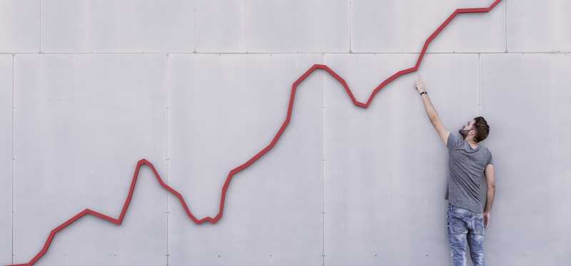 Male looking at red trend line shooting upward on wall