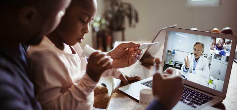 Parent and child taking child's temperature as they consult with doctor through a video call