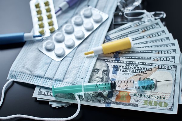 Pills and face mask on table with syringes and hundred dollar bills.