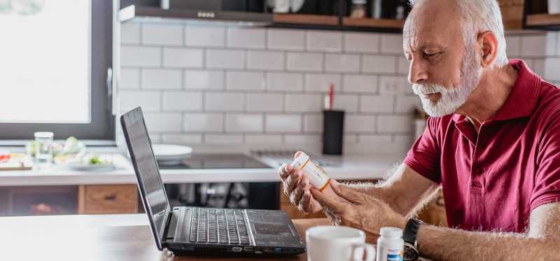 Retired man sitting at kitchen table and looking at prescription bottles