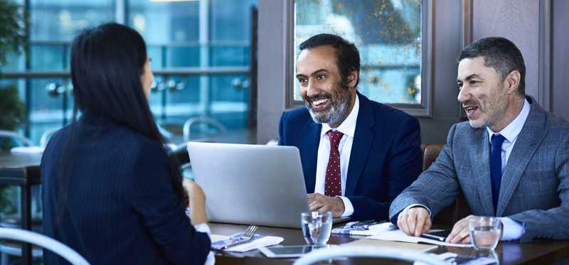 Smiling businesspeople talking and reviewing data on laptop.