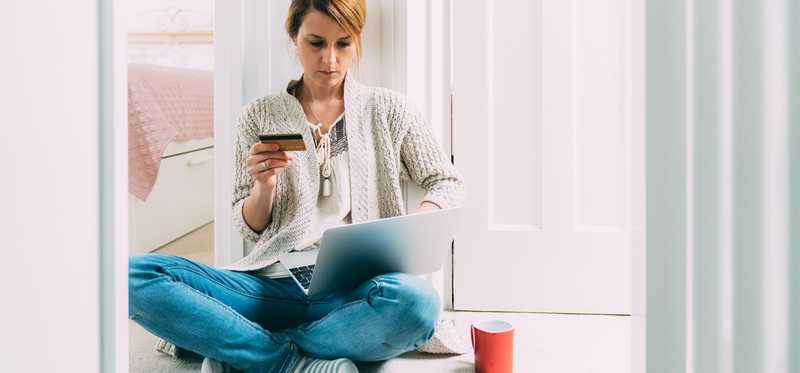 Woman sitting on floor about to make online purchase on laptop with her credit card