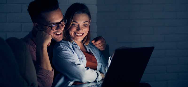 Couple smiling and watching movie on laptop