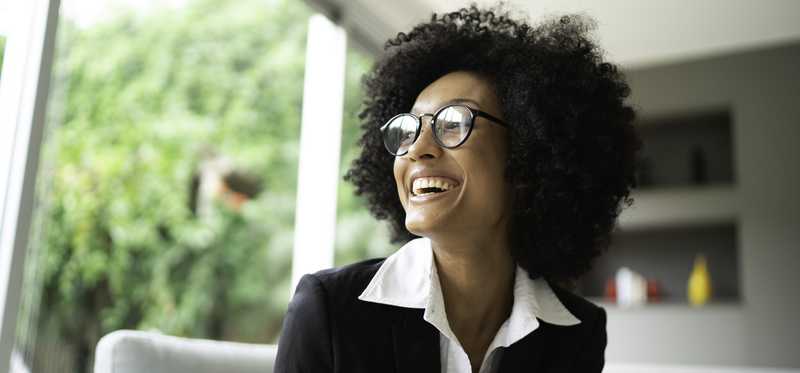 Smiling person sitting on couch and looking out the window. to green space.