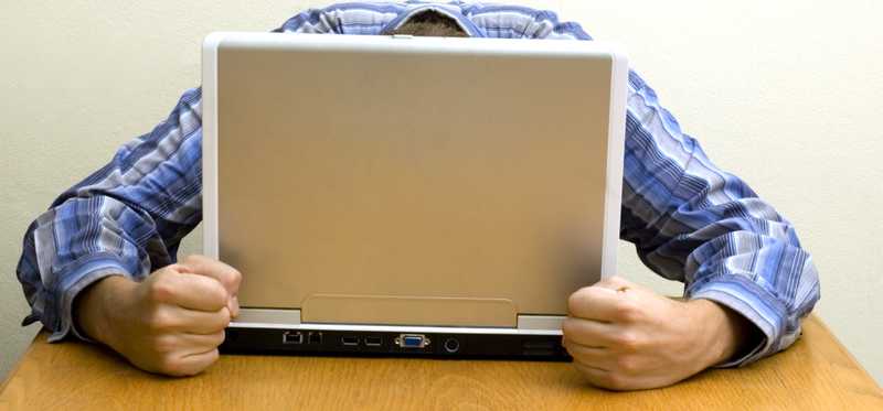 Frustrated person hides face in laptop.