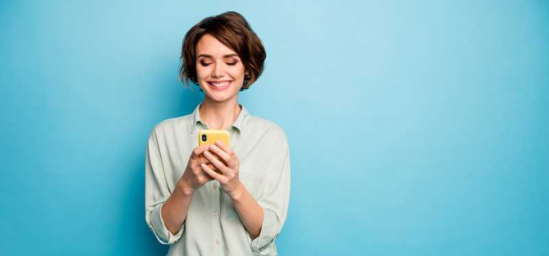 Woman looking at smartphone and standing in front of blue background