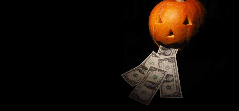 Jack-o-lantern with dollar bills near its mouth.