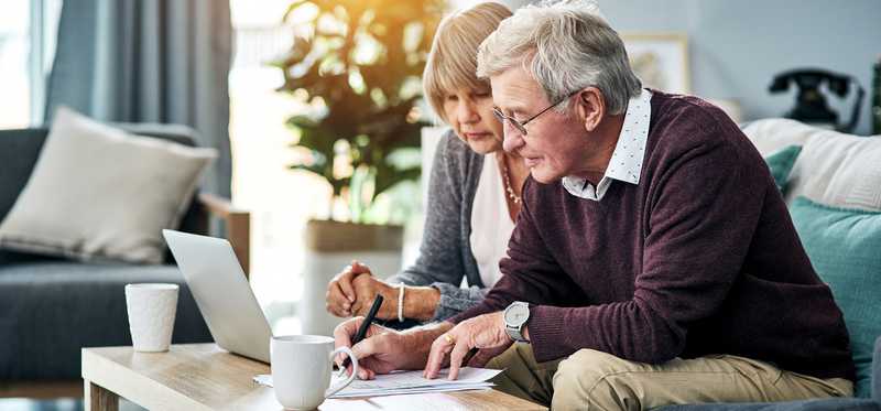 Two people sitting on couch and looking at laptop and documents.