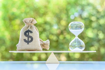 Bags with dollar sign balanced next to hourglass.