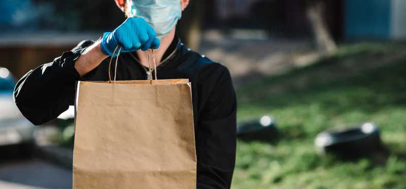 Delivery worker wearing mask and holding paper bag of food.