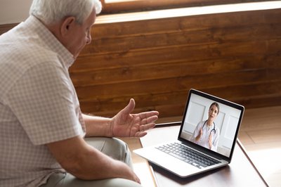 Person sitting at computer attending telehealth consultation with doctor.