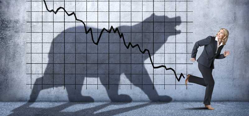 Person running away from shadow of bear on background of declining arrow on graph.