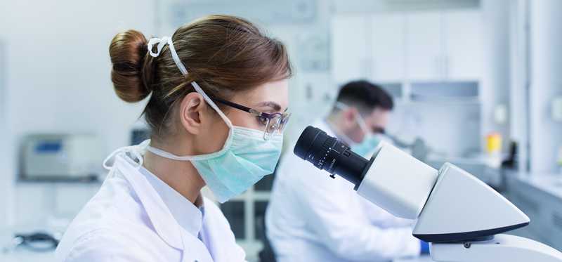 Scientists in masks and lab coats, examining specimens through microscopes.