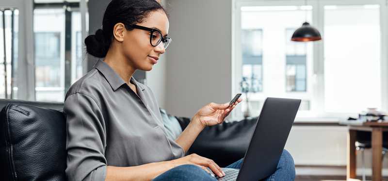 Person sitting on couch and getting ready to make online purchase while looking at laptop and holding credit card.