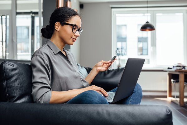 Person sitting on couch and getting ready to make online purchase while looking at laptop and holding credit card.