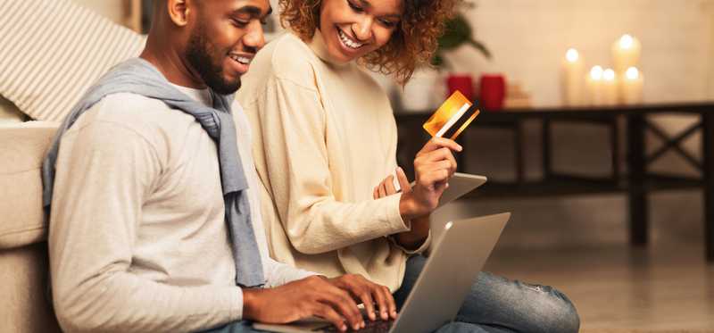 Couple sitting at laptop with the woman holding credit card and preparing to make purchase