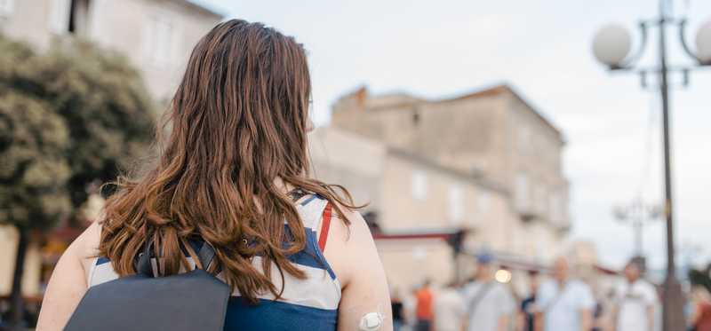 Young woman wearing continuous glucose monitoring device and backpack exploring city