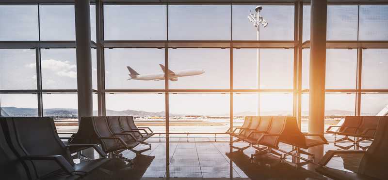 Empty sun-filled gate waiting area in airport with plane taking off in the distance