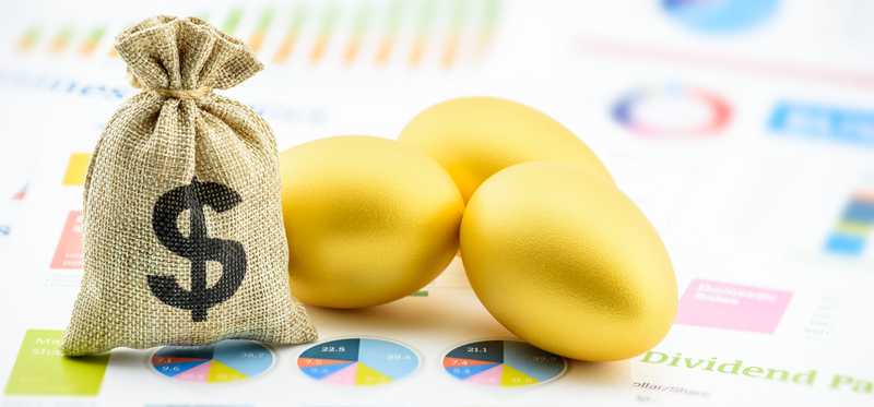 Golden eggs and small burlap bag with dollar sign all lying on financial charts