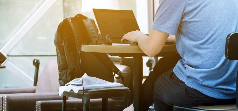 Person sitting at table with laptop and backpack while remote working.